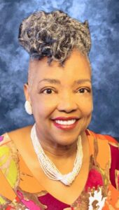 Dr. Iris Davis smiling at the camera in front of a formal blue background wearing a bright top